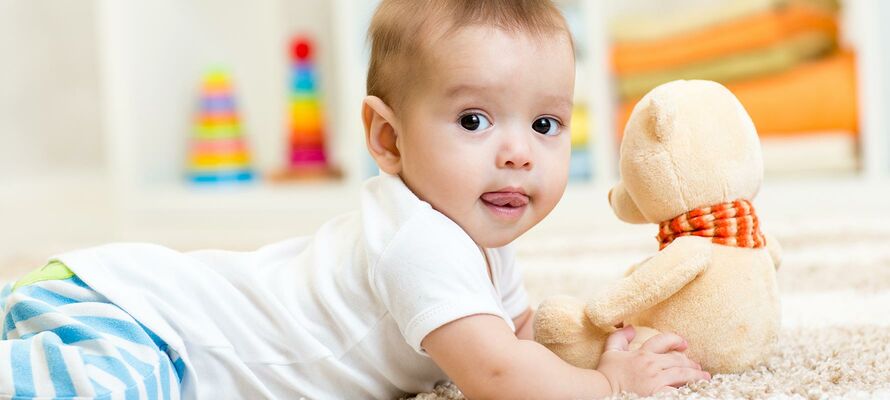 am Bauch liegendes bekleidetes Baby mit Stoffbär